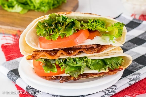 Close up picture of a white plate with a BLT tortilla wrap stuffed with bacon, lettuce, and tomatoes on it