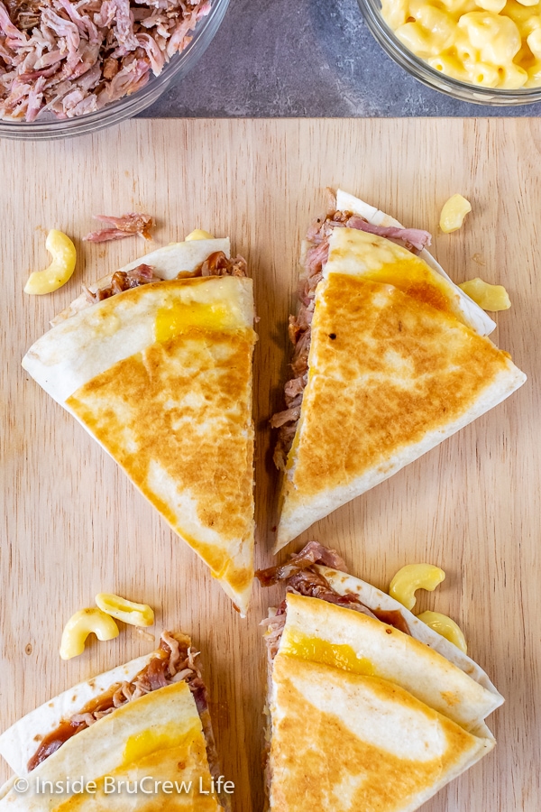 Overhead picture of a cutting board with pulled pork macaroni and cheese tortilla wraps cut in half on it