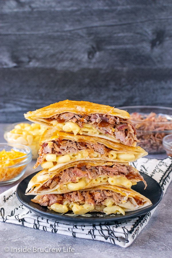 A black plate on a towel with pulled pork macaroni and cheese wraps cut in half and stacked on top of each other showing the filling