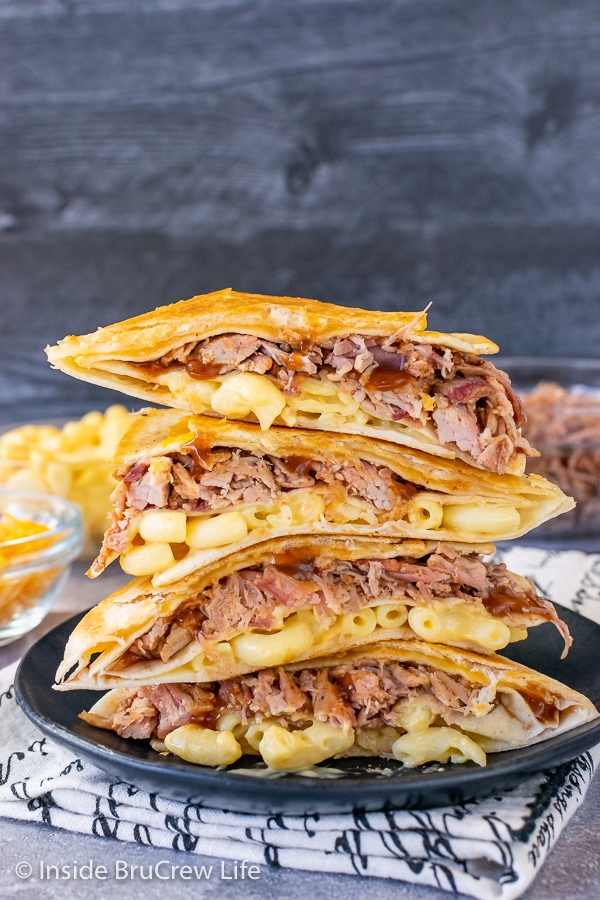 Four pulled pork macaroni and cheese tortilla wraps stacked on top of each other on a black plate showing the inside fillings