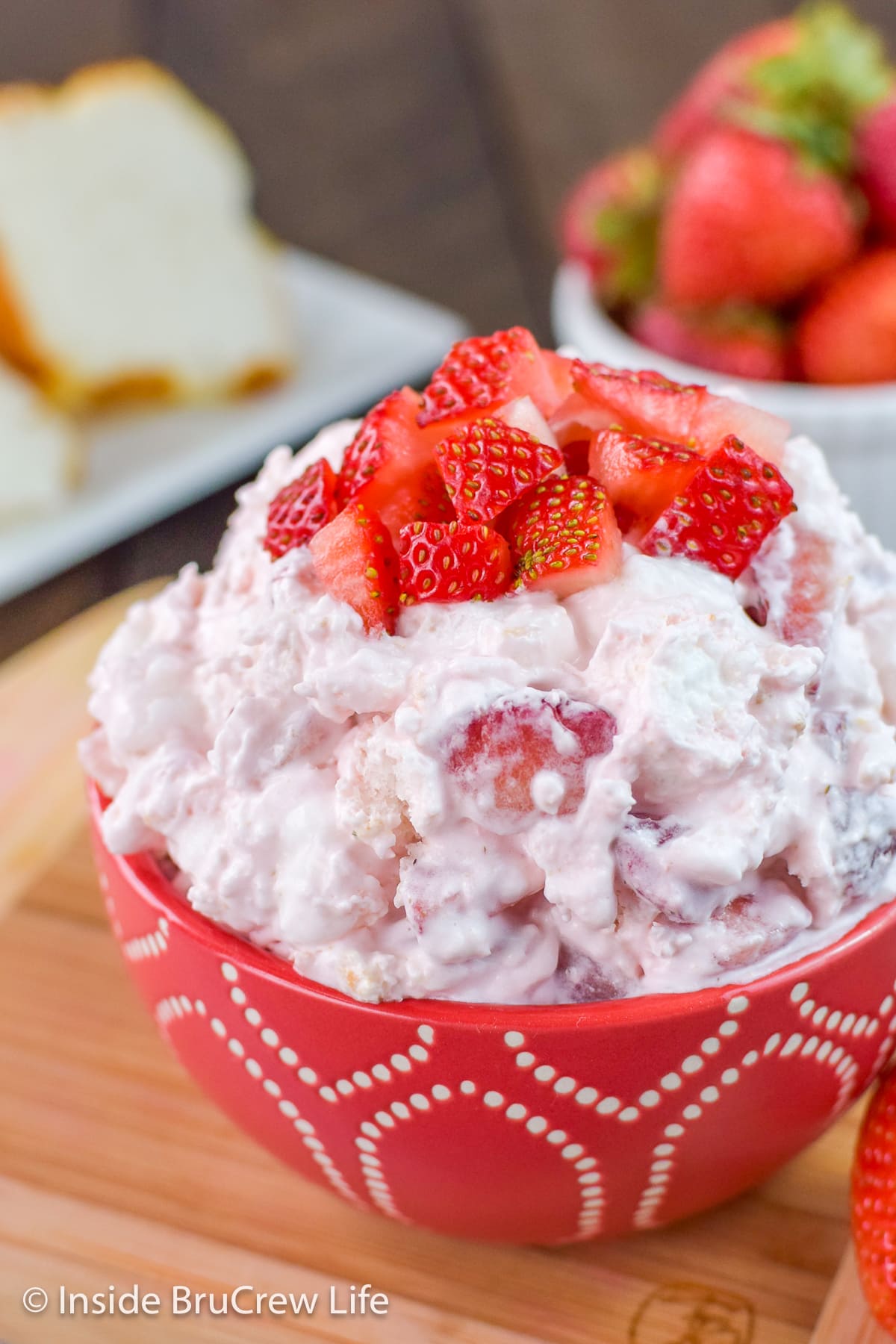 A red bowl filled with pink dessert salad and topped with fresh strawberries.