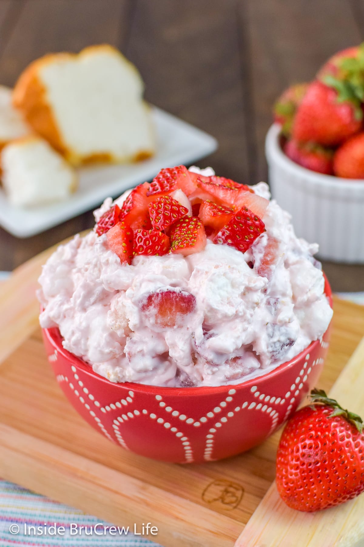 A red bowl filled with strawberry fluff salad and topped with fresh berries.