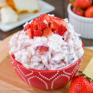 A red bowl filled with strawberry fluff salad and topped with fresh berries.