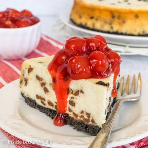 A slice of chocolate chip cheesecake topped with cherry pie filling on a white plate