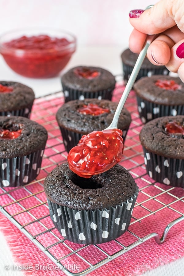 A dark chocolate cupcake with a spoonful of raspberry pie filling being dropped into the center