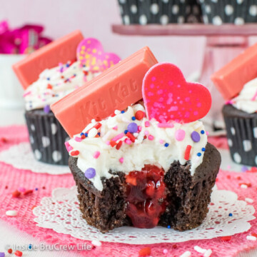 A chocolate cupcake with vanilla frosting with a bite take out of it showing the raspberry filling