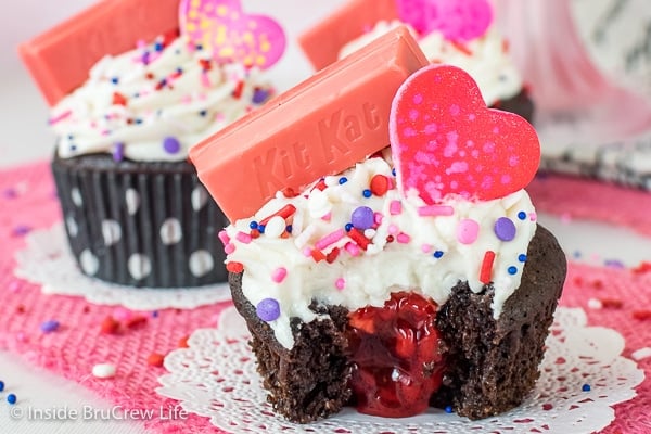 Close up of a chocolate cupcake frosted with vanilla buttercream with a bite taken out showing the raspberry center