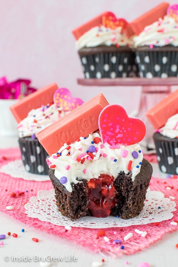 Two chocolate cupcakes topped with vanilla frosting and sprinkles with a bite out of one showing a raspberry filling center
