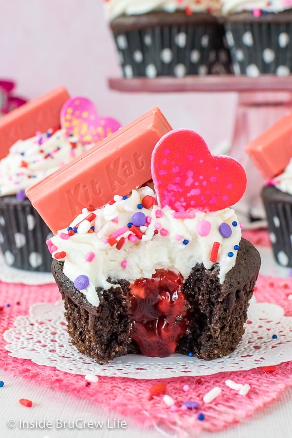 A chocolate cupcake frosted with vanilla frosting with a bite taken out to show the raspberry pie filling center