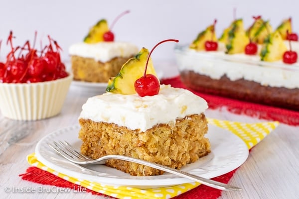 A white plate with a square of homemade pineapple cake topped with pineapple frosting and cherries