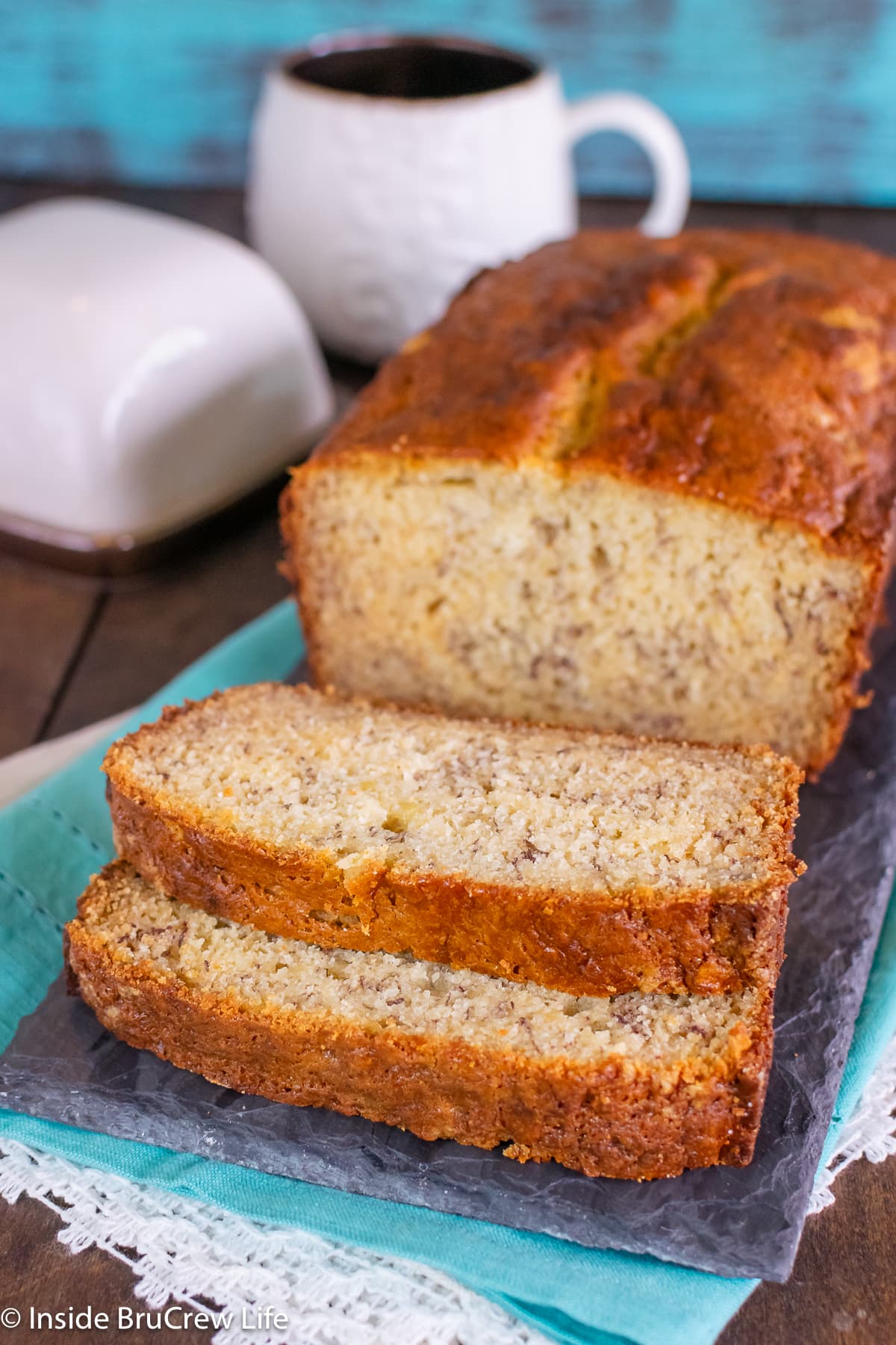 A loaf of quick bread with two slices on a dark board.