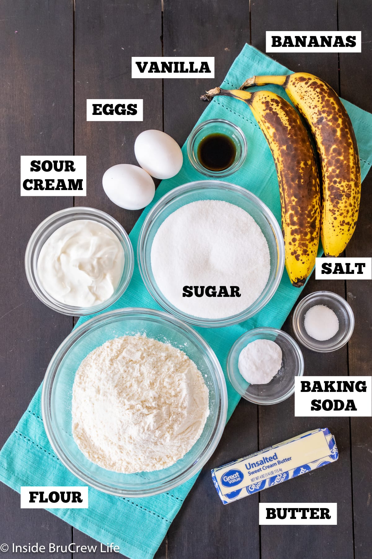A dark board with bowls of ingredients needed to make banana bread.