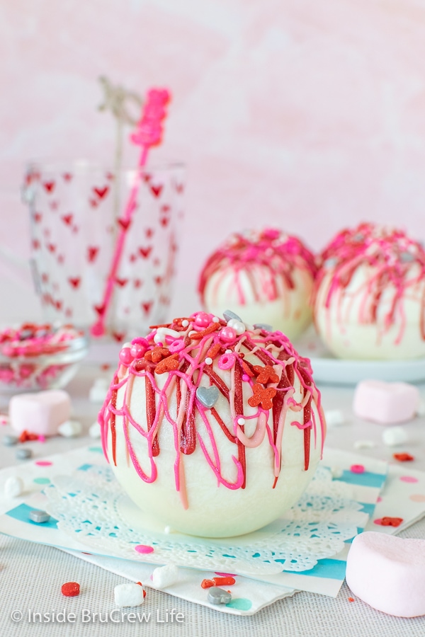 A white doily with a strawberry white hot chocolate bomb drizzed with red and pink chocolate on it