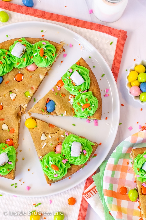 An overhead picture of a white plate with slices of Easter cookie cake with frosting and sprinkles on it.