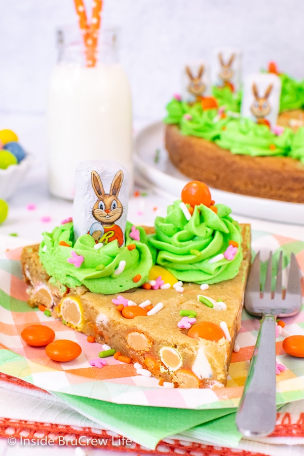 A slice of cookie cake with green frosting and chocolate bunnies on a  plate.