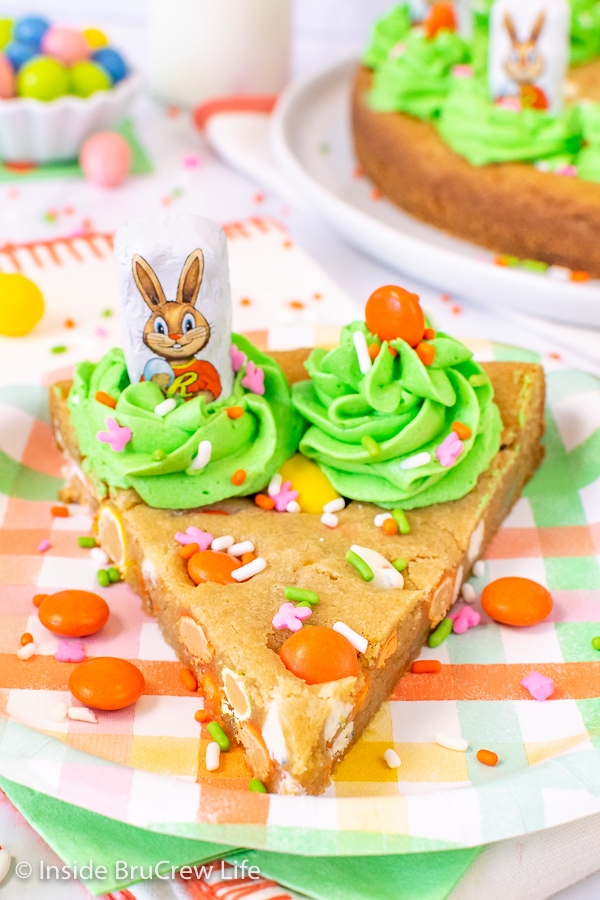 A slice of decorated cookie cake on a pastel plate with green swirls and candies on it