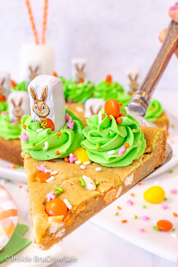 A slice of a decorated cookie cake being lifted on a spatula over the whole cake.