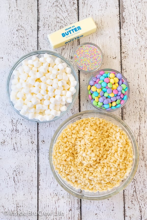 A white board with the ingredients to make Easter rice krispies treats in bowls