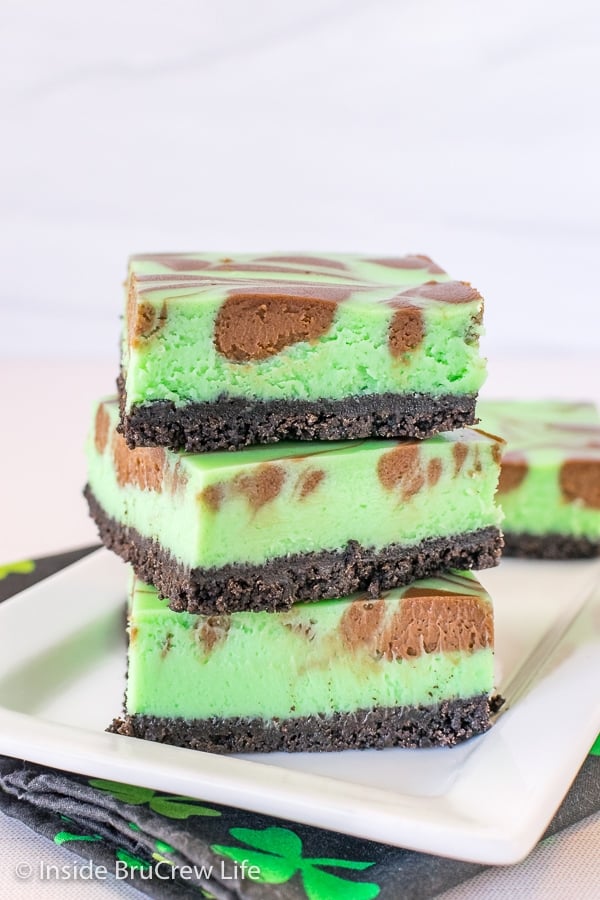 A stack of three grasshopper cheesecake bars with chocolate swirls on a white plate