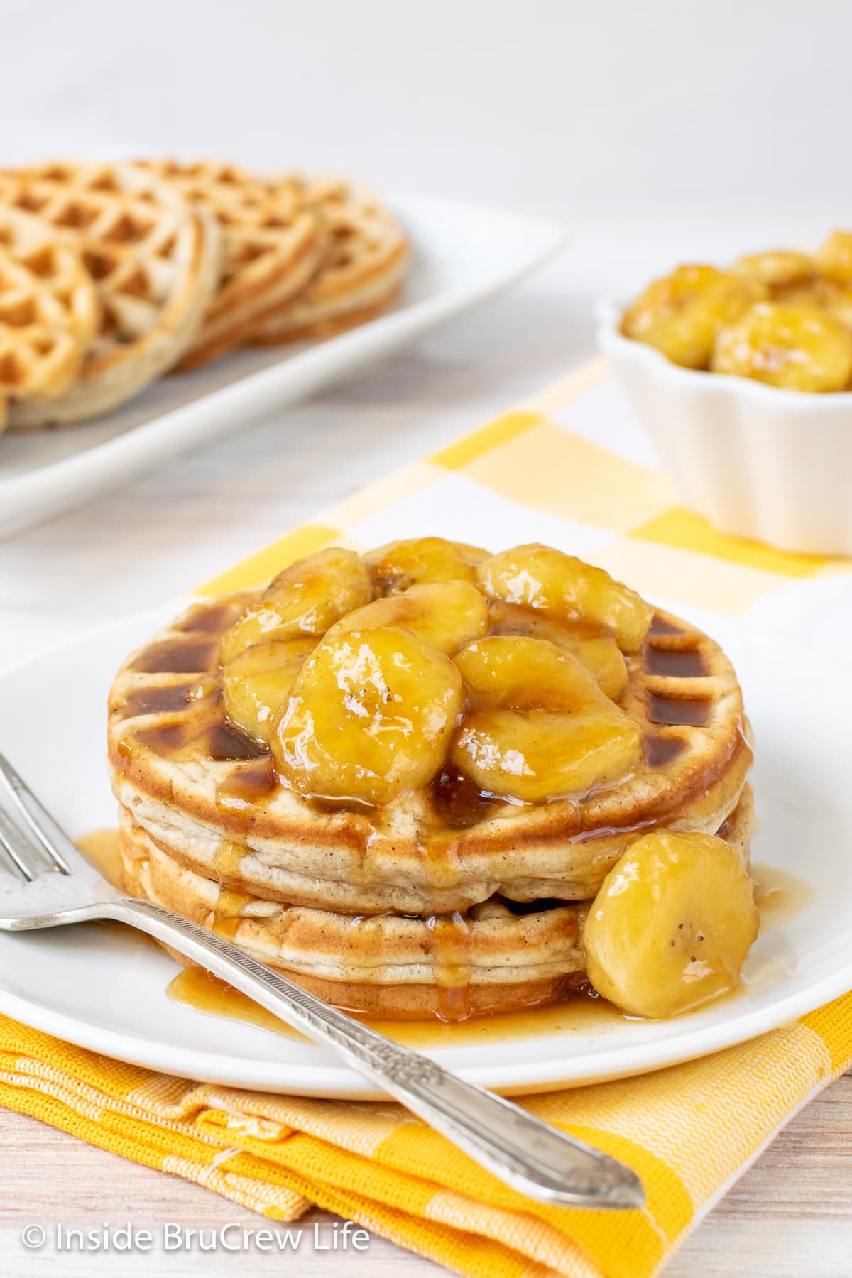 Two waffles topped with caramel bananas on a white plate.