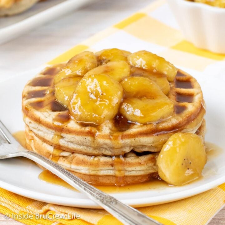 Two waffles topped with caramel bananas on a white plate.