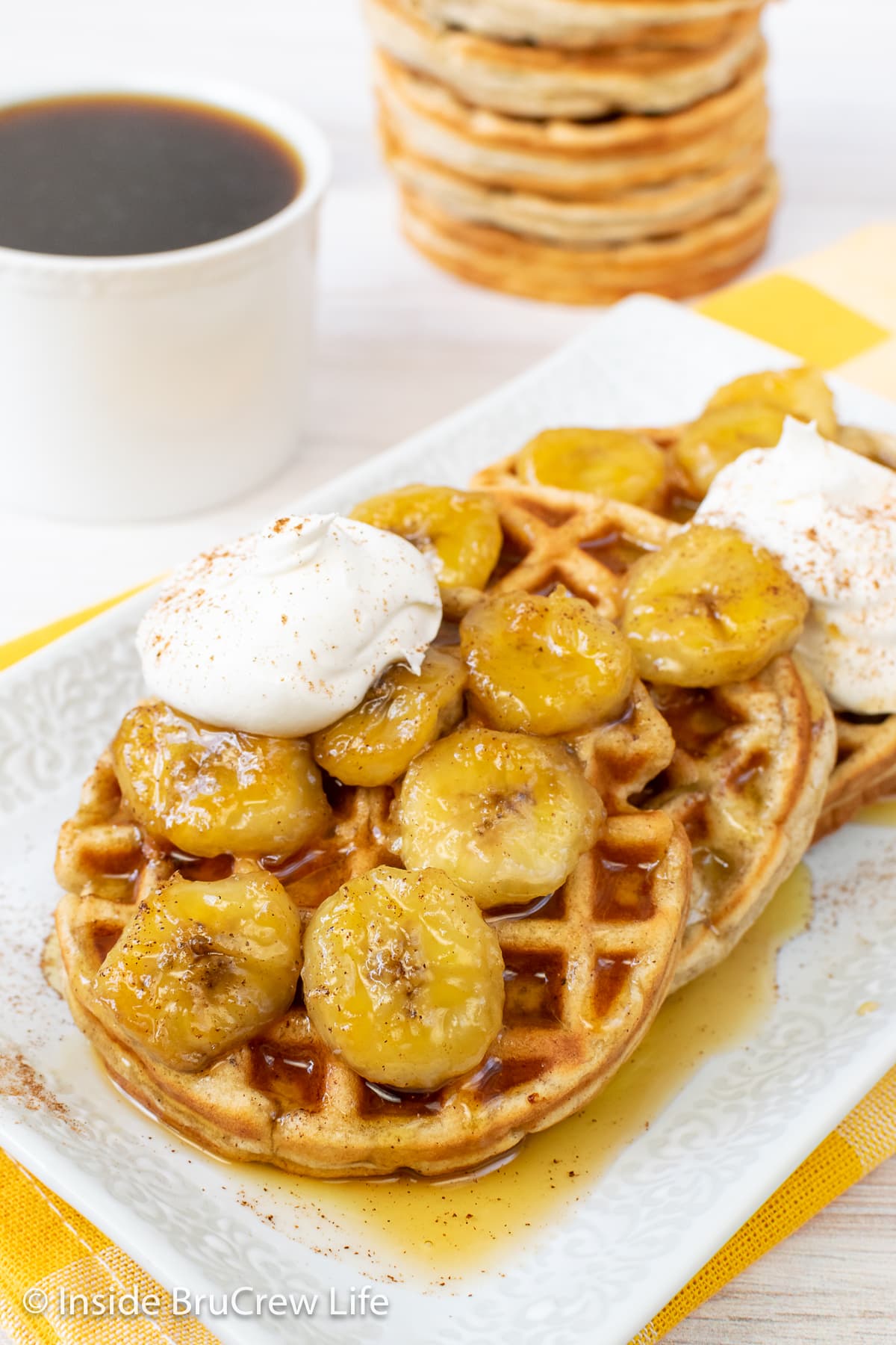 Waffles on a white plate topped with syrup, bananas, and whipped cream.