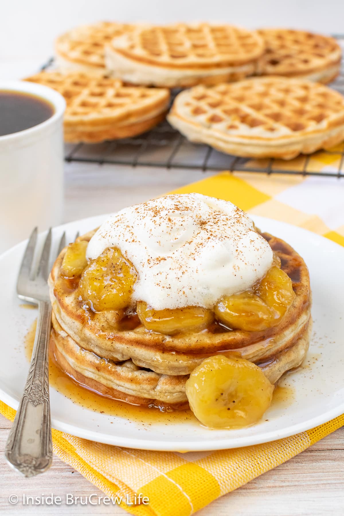 Waffles on a white plate topped with bananas and whipped cream.