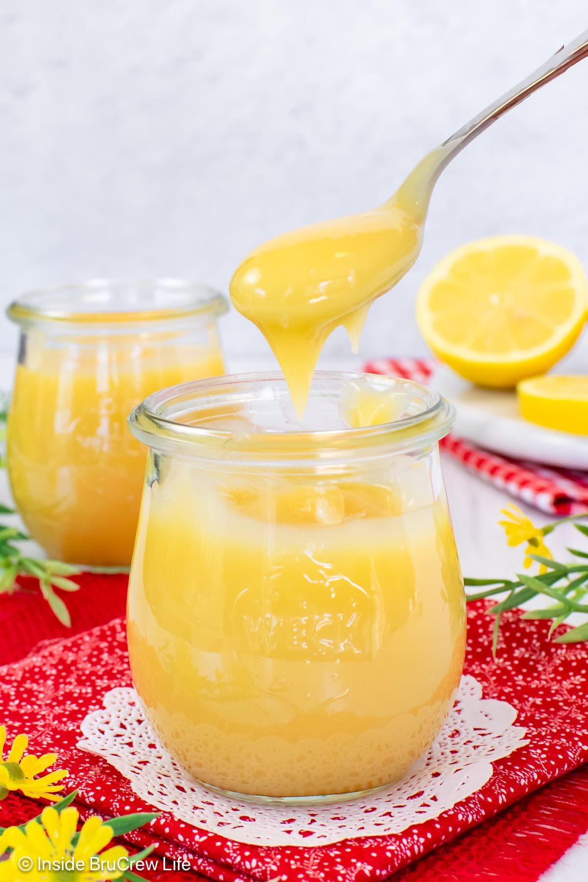 A spoon lifting lemon curd out of a clear jar.