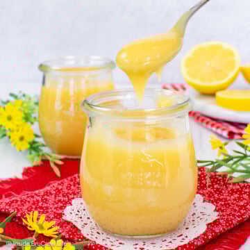 A spoon lifting lemon curd out of a clear jar.