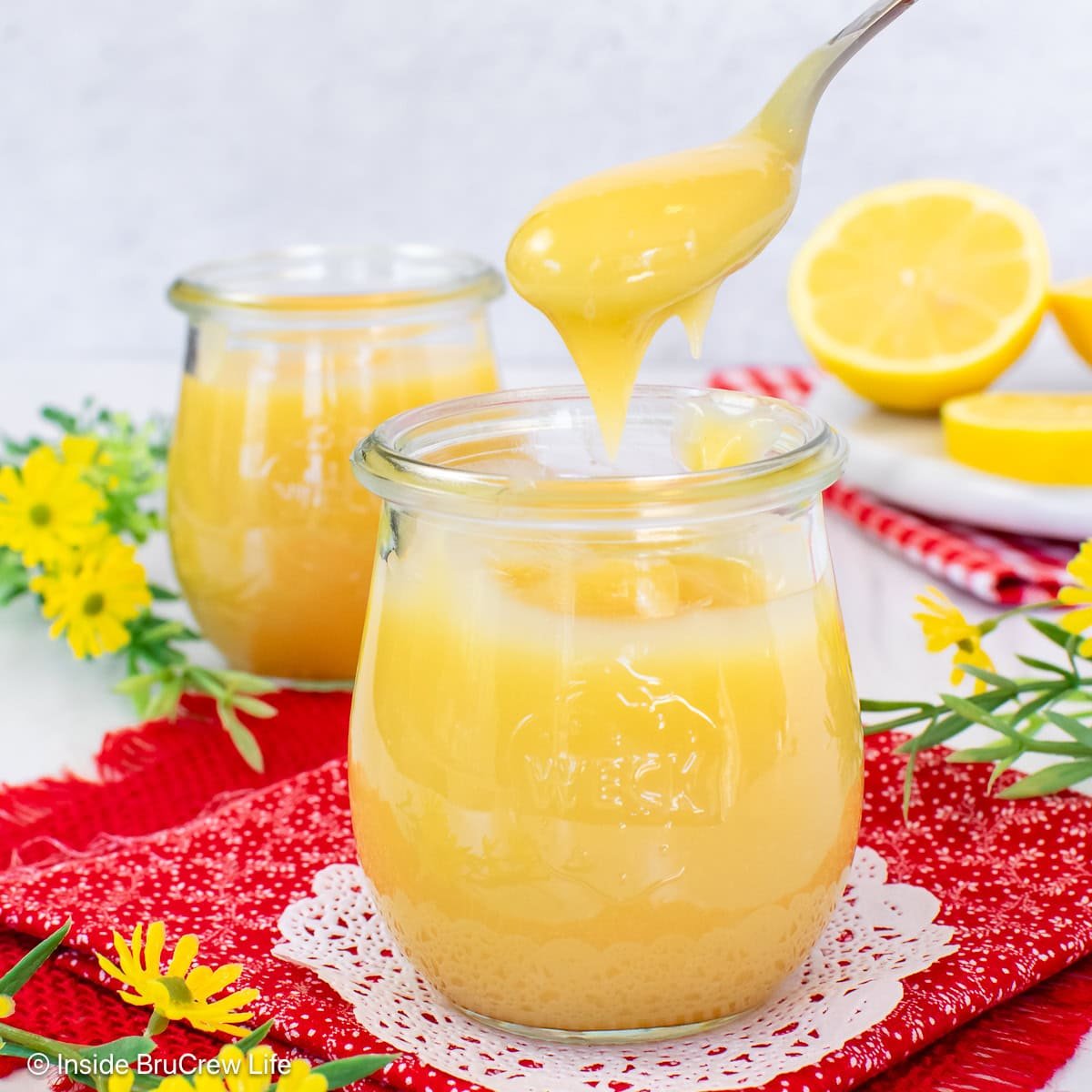 A spoon lifting lemon curd out of a clear jar.