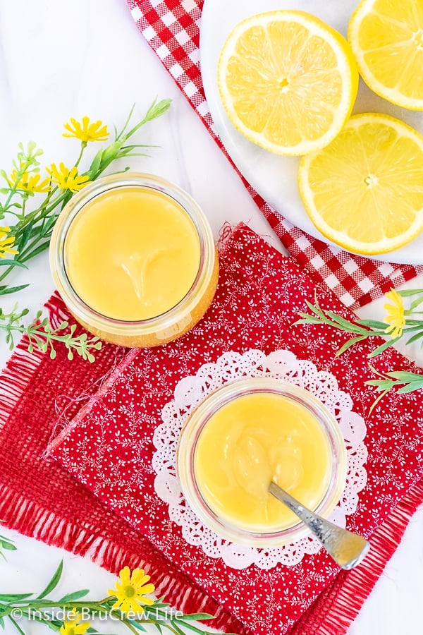 Overhead picture of a red towel with two jars filled with lemon curd on it and lemon slices beside them