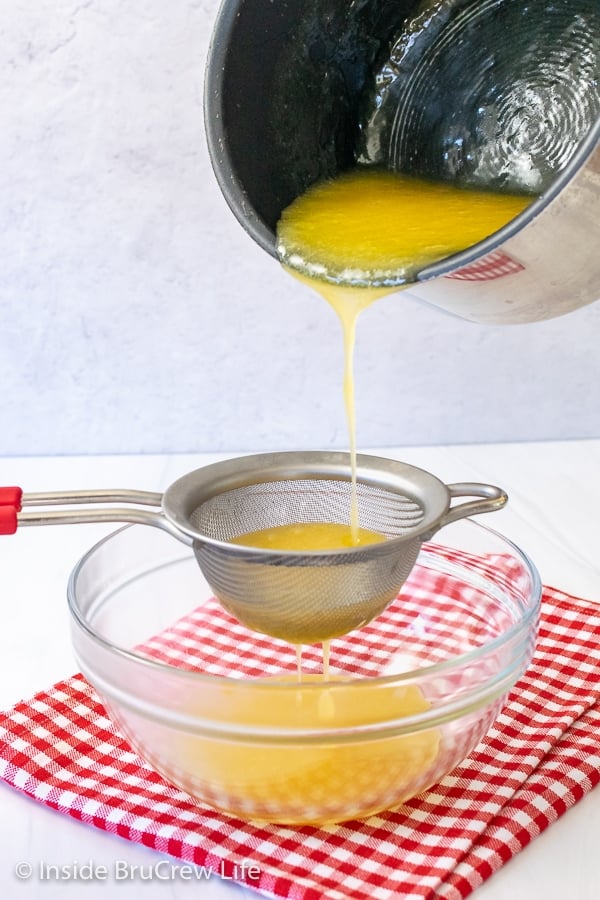 A pan of lemon curd being poured into a strainer over a bowl on a red and white towel