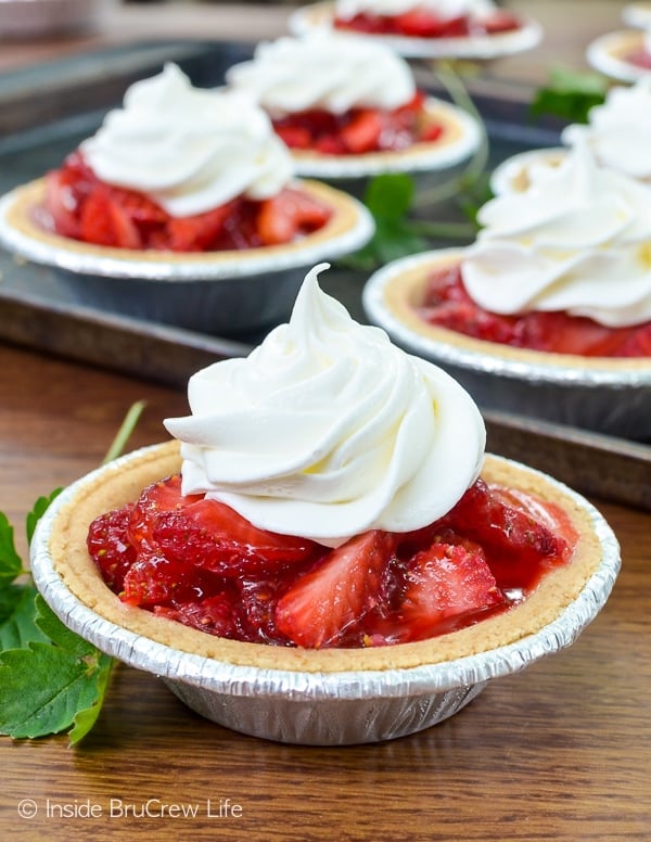 A mini strawberry pie topped with whipped cream and a tray of pies behind it