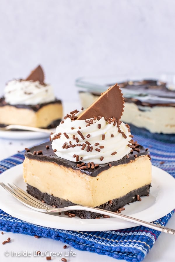 Two white plates on a blue towel with peanut butter pie bars topped with whipped cream, sprinkles, and peanut butter cups on them