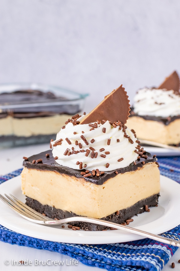 A white plate with a square of peanut butter pie bars topped with whipped cream and a peanut butter cup on it