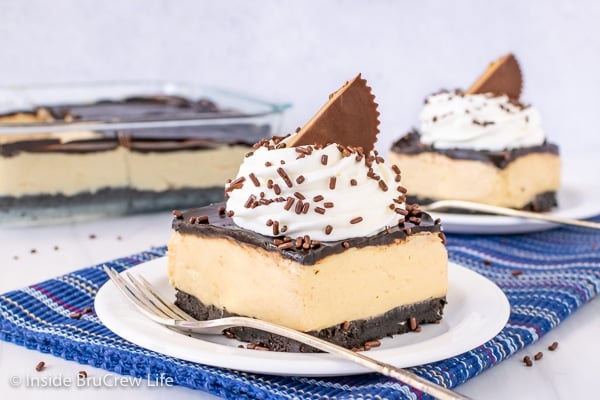 Two white plates with peanut butter squares topped with chocolate, whipped cream, and peanut butter cups on them