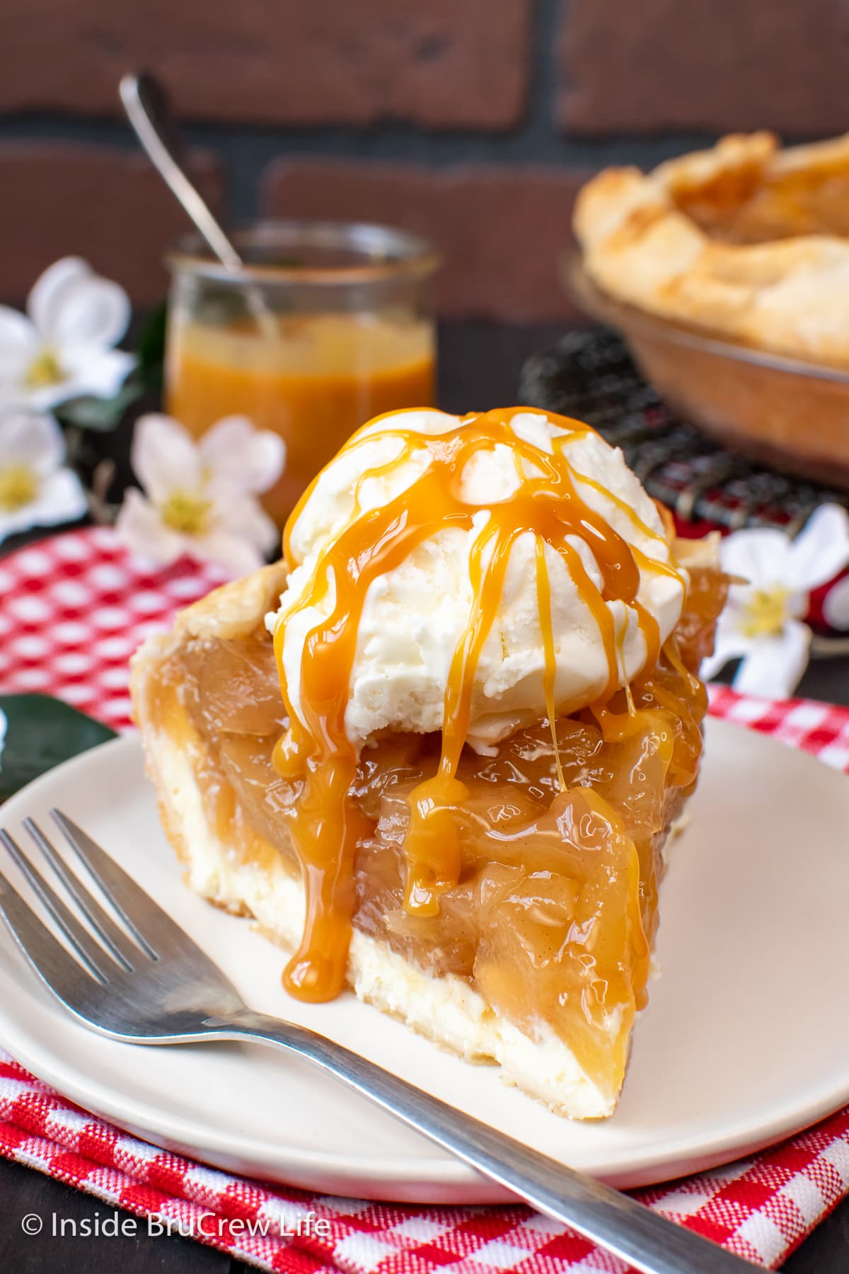 A slice of cheesecake pie with apples on a plate drizzled with caramel.