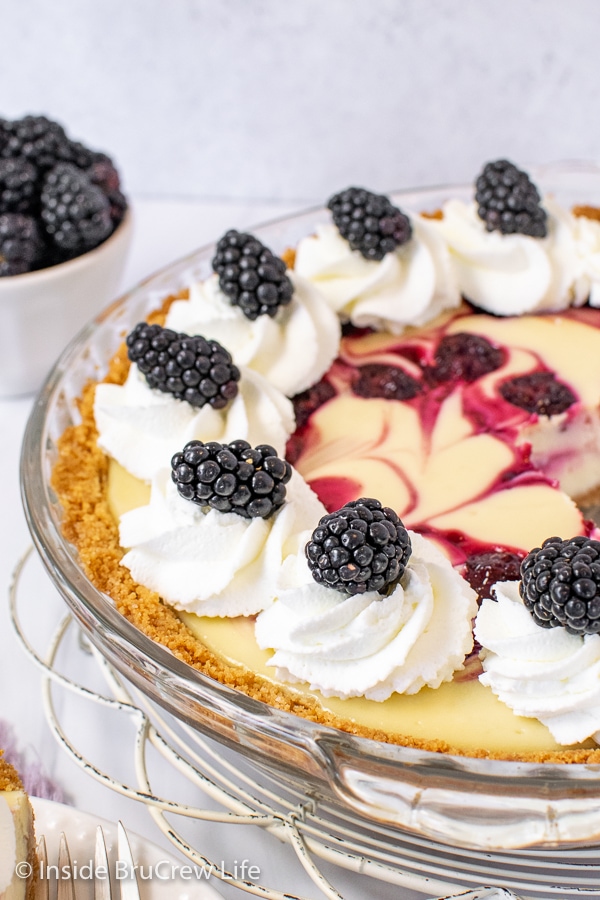 A close up of the side of a cheesecake pie with whipped cream swirls and fresh blackberries