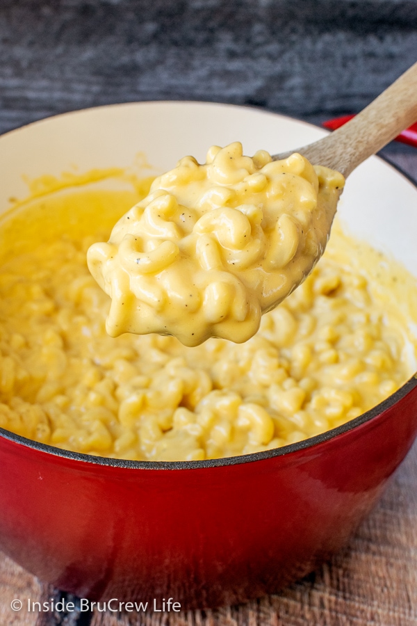 A red pot filled with creamy mac and cheese and spoon lifting some out