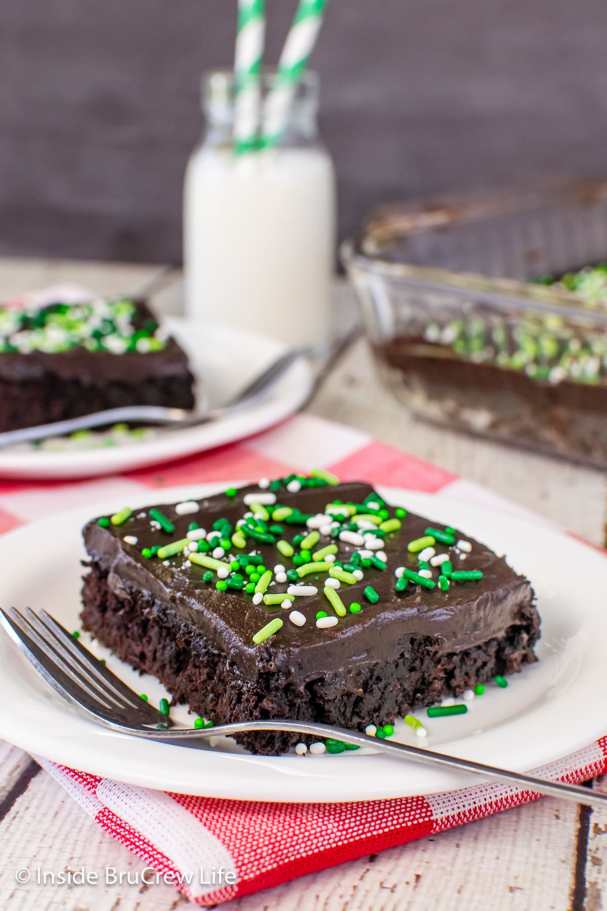 Two white plates with squares of chocolate cake on them.