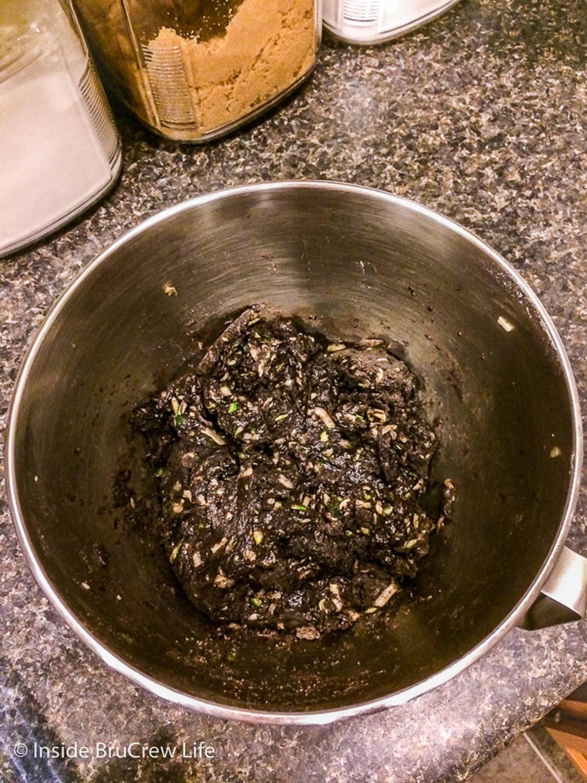 A metal bowl with the wet dough needed to make a chocolate cake with zucchini.