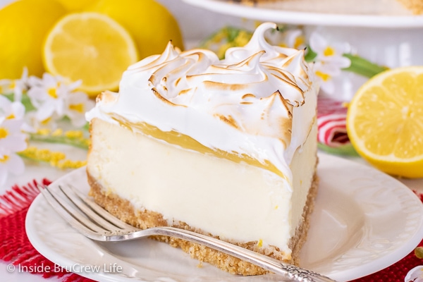 A white plate on a red towel with a slice of lemon meringue cheesecake and a fork on it.