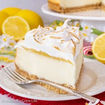 A white plate with a slice of lemon cheesecake topped with lemon curd and marshmallow meringue on it