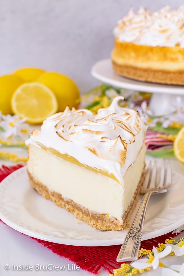 A slice of lemon cheesecake topped with lemon curd and meringue on a white plate.