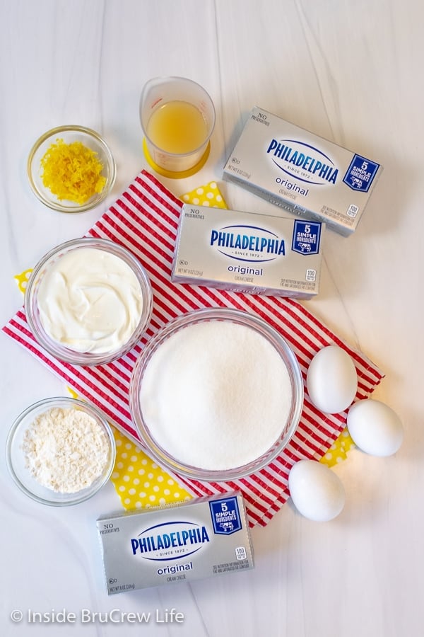 A white board with bowls filled with ingredients needed to make lemon cheesecake on it.