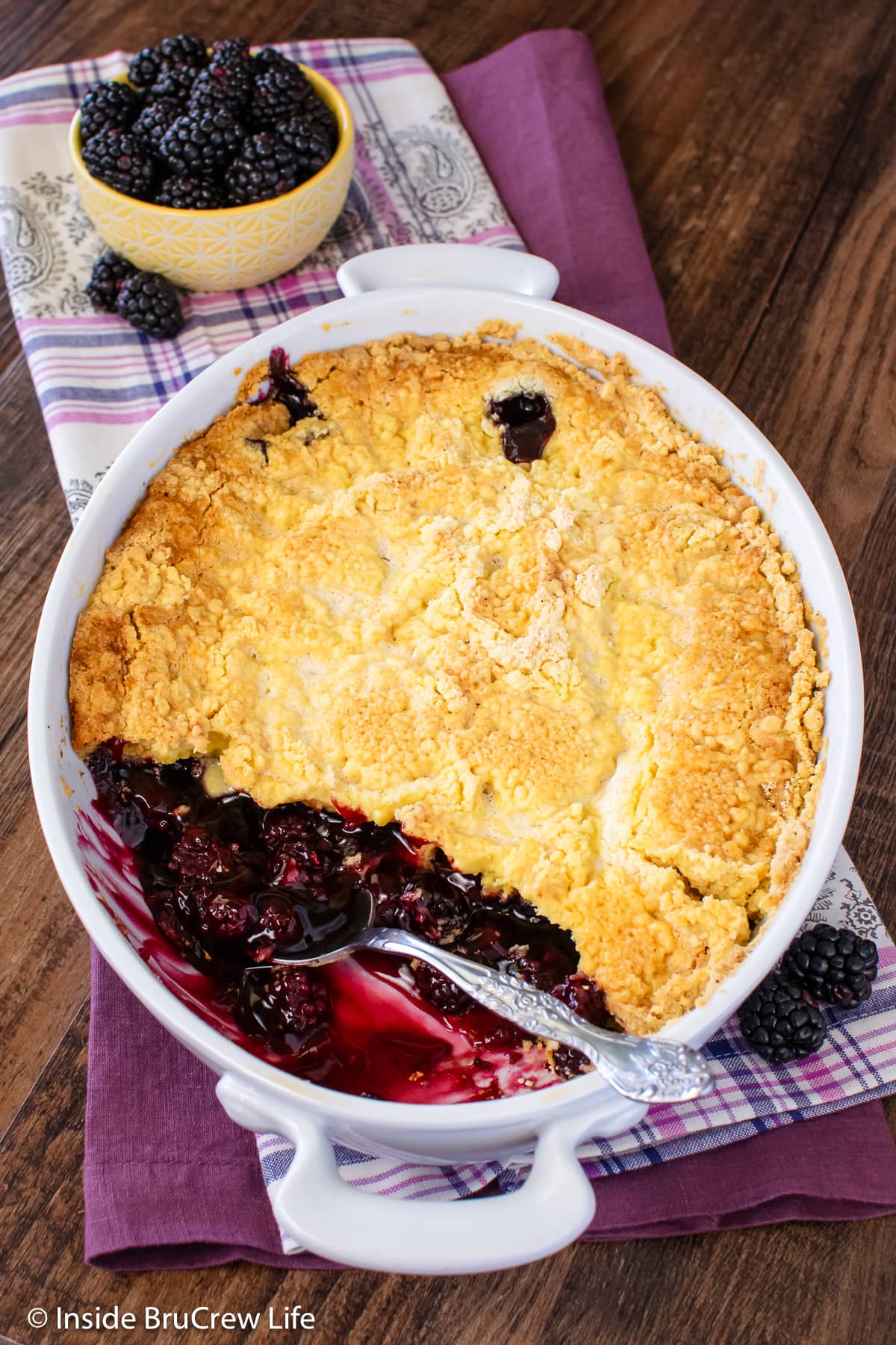 A white dish with fruit cobbler in it and a big scoop missing.