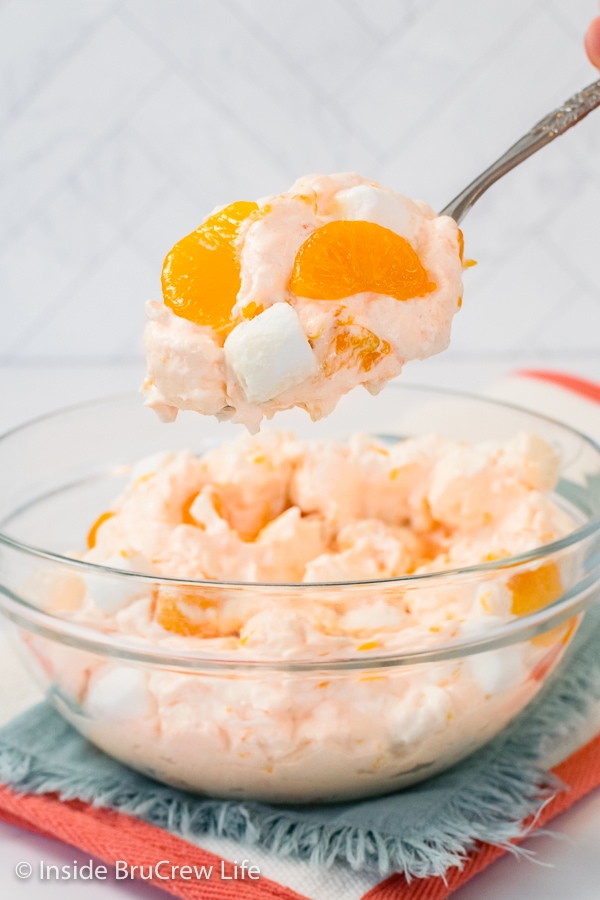 A bowl of orange fluff salad on a blue towel with a spoon lifting a scoop out.