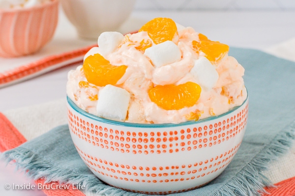 A blue towel with a white and orange bowl on it that is filled with orange fluff salad.