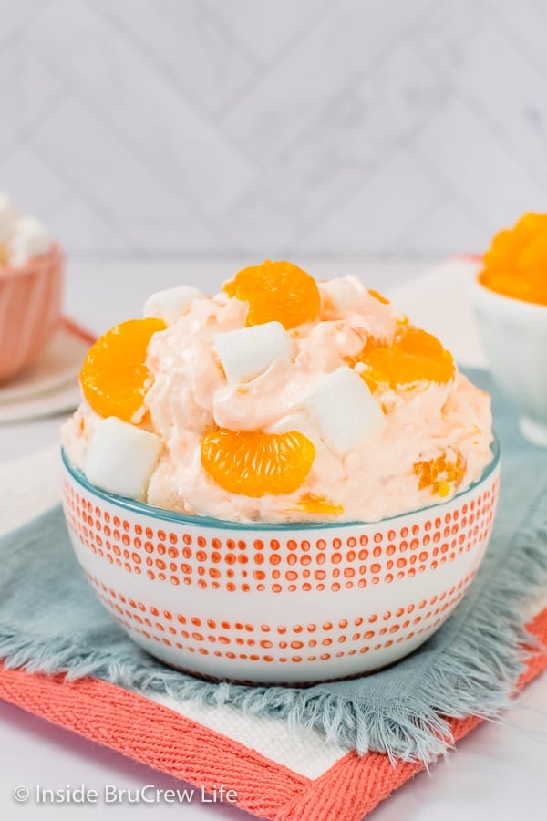 A white and orange bowl on a blue towel filled with Orange Fluff and topped with extra oranges.