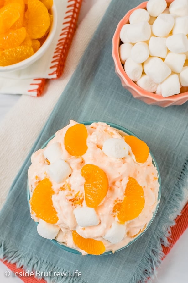 Overhead picture of a bowl filled with orange Jello salad on a blue towel.